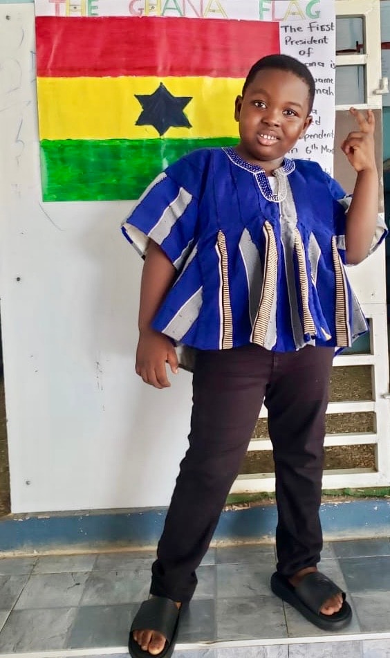 Boy in traditional blue Ghanaian smock posing proudly in front of the Ghana flag
