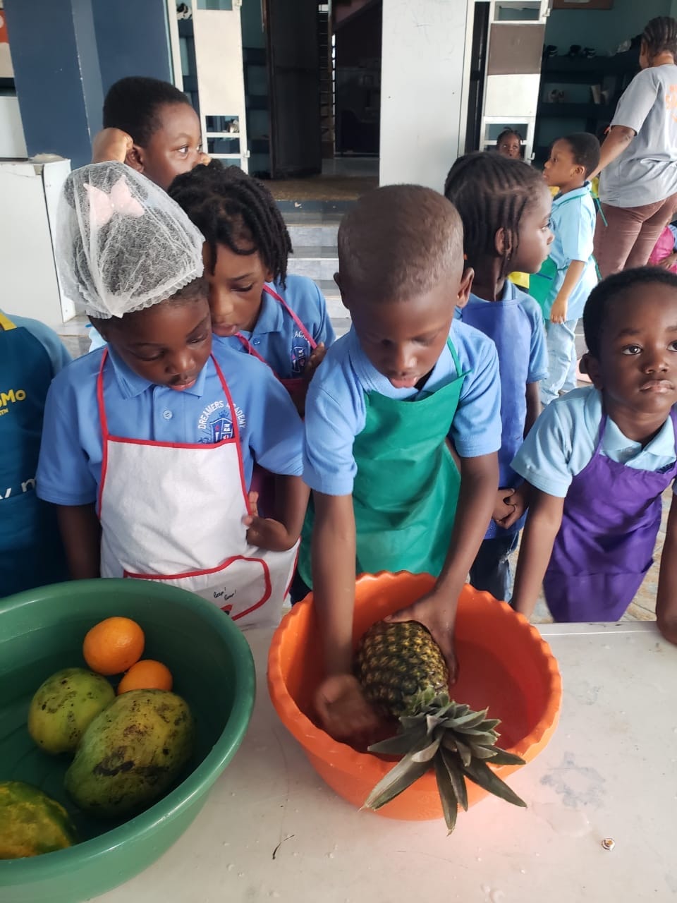 Student in hair net washing mangoes in a bowl