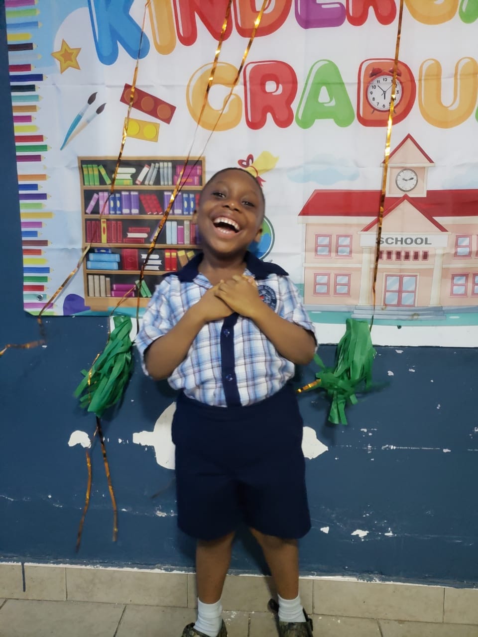 Joyful young graduate laughing in front of the Kindergarten Graduate banner