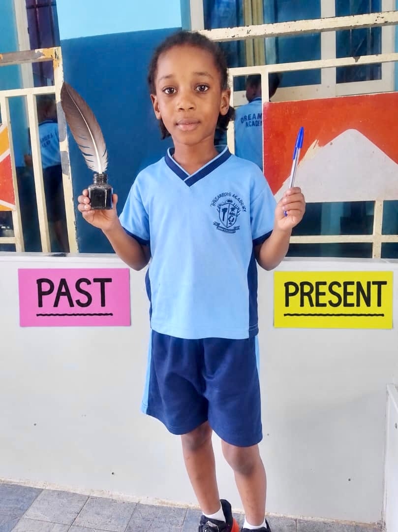 Student holding a feather quill and ink (past) and a ballpoint pen (present)