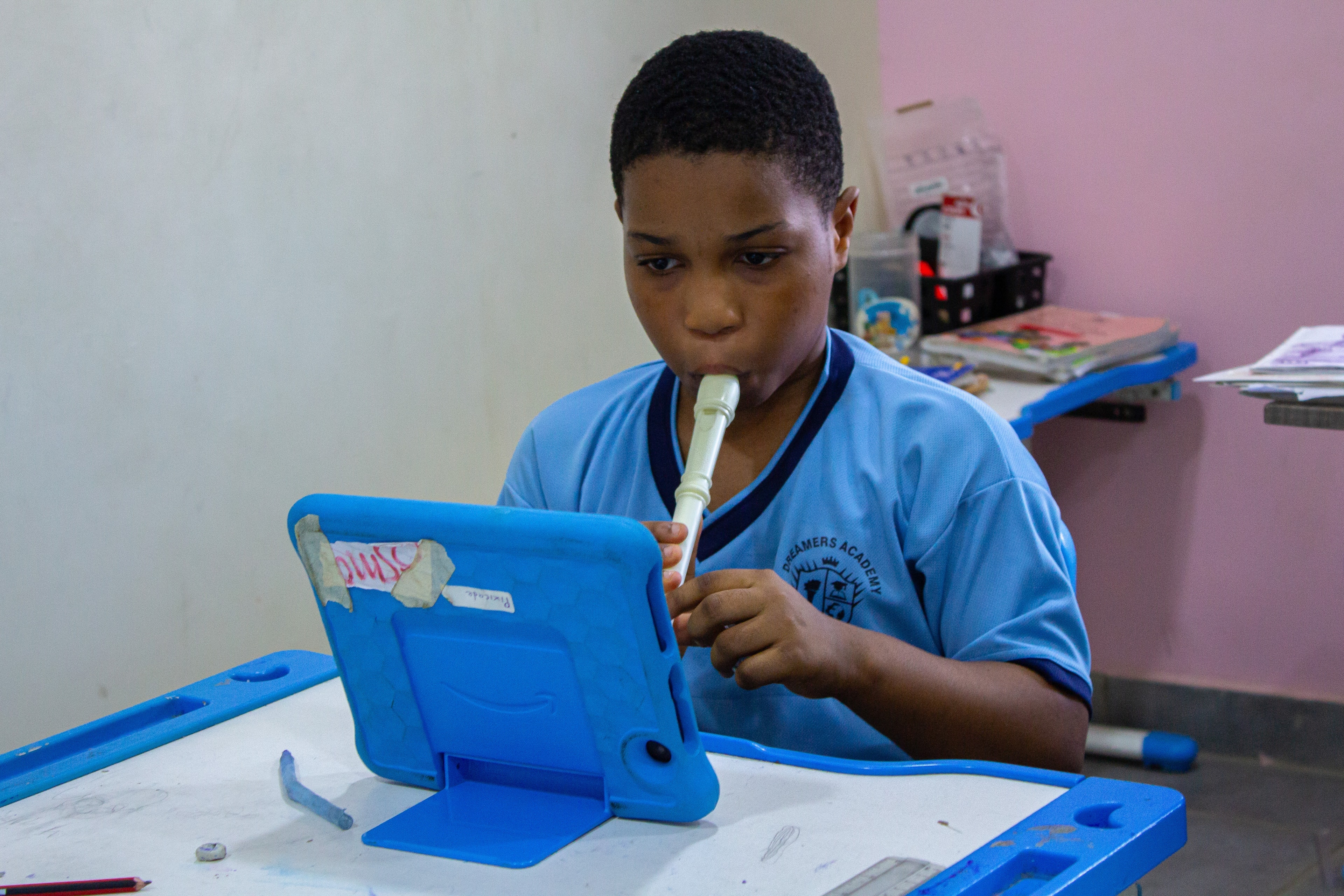 Dreamers Academy-GH student playing recorder at his desk with a tablet